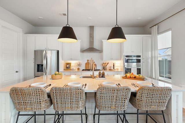 kitchen featuring wall chimney exhaust hood, appliances with stainless steel finishes, and a breakfast bar area