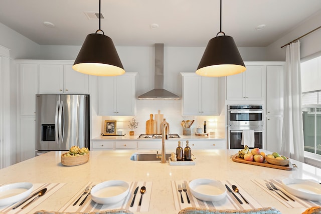 kitchen featuring light stone counters, wall chimney range hood, pendant lighting, and appliances with stainless steel finishes