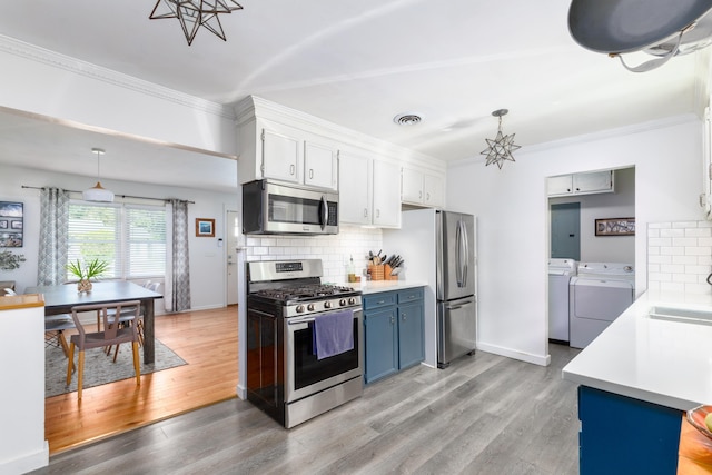 kitchen featuring white cabinets, washing machine and dryer, appliances with stainless steel finishes, and hanging light fixtures