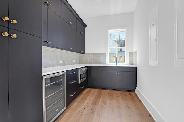 kitchen featuring sink, stainless steel microwave, beverage cooler, light hardwood / wood-style flooring, and backsplash