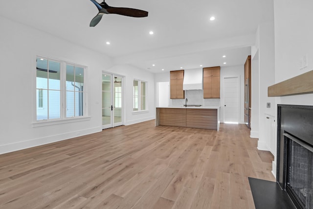 unfurnished living room featuring ceiling fan, light wood-type flooring, and sink