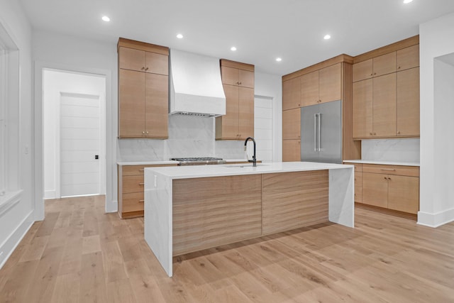 kitchen with premium range hood, sink, light hardwood / wood-style flooring, built in refrigerator, and tasteful backsplash