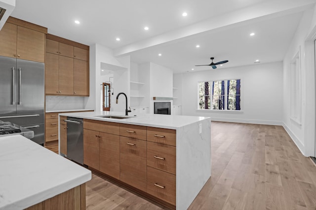 kitchen with a large island, sink, ceiling fan, built in fridge, and light hardwood / wood-style floors