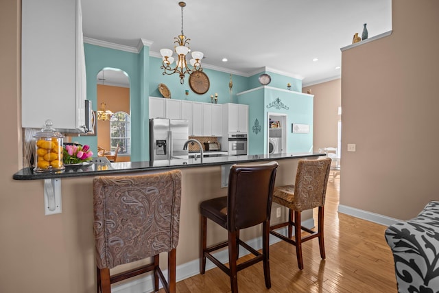 kitchen featuring dark countertops, white cabinetry, stainless steel appliances, a peninsula, and a chandelier