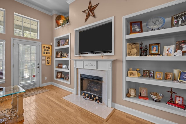 living room with built in shelves, wood finished floors, baseboards, a high end fireplace, and ornamental molding