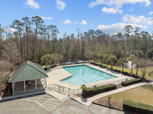 community pool with a wooded view, a patio, and fence