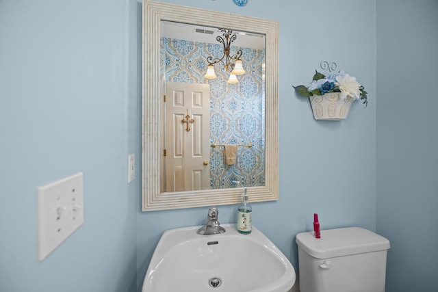 half bath with a sink, a notable chandelier, and toilet