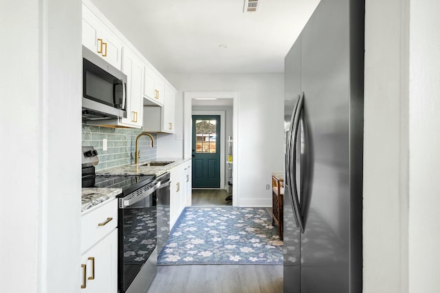 kitchen featuring appliances with stainless steel finishes, light stone counters, decorative backsplash, a sink, and wood finished floors
