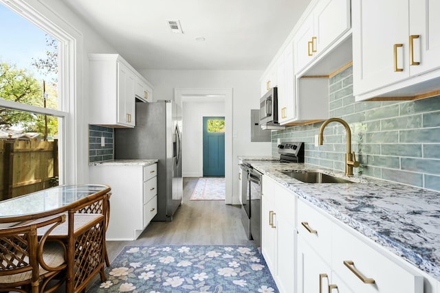 kitchen with visible vents, a sink, white cabinetry, light stone countertops, and stainless steel appliances