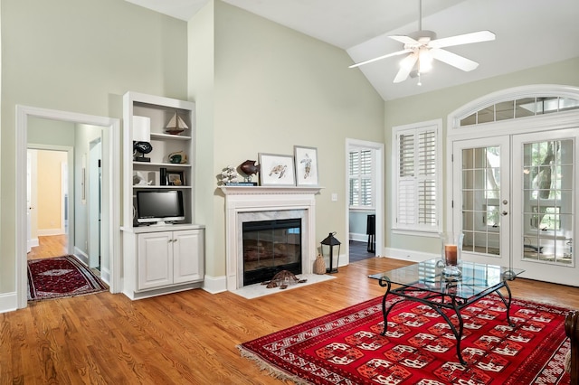 living area with light wood-type flooring, high vaulted ceiling, a fireplace, and a ceiling fan