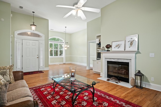 living room with visible vents, baseboards, a fireplace, light wood finished floors, and ceiling fan with notable chandelier