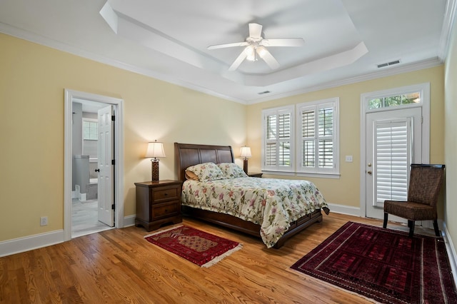 bedroom with ornamental molding, visible vents, a raised ceiling, and wood finished floors