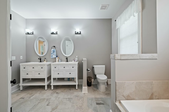 full bath with vanity, baseboards, toilet, visible vents, and a tub to relax in