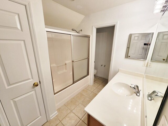 full bathroom with vanity, lofted ceiling, combined bath / shower with glass door, tile patterned flooring, and toilet