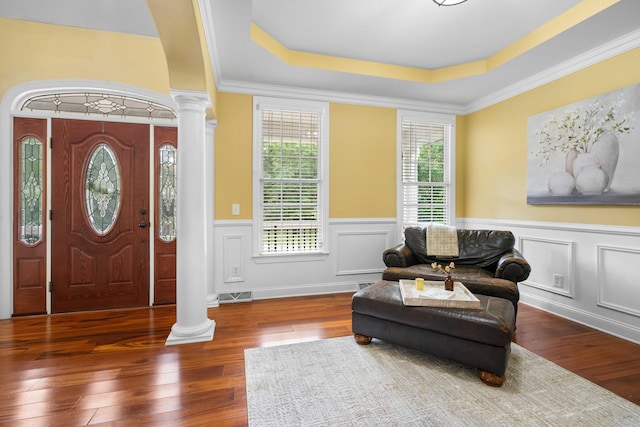 entryway with dark wood-type flooring, ornamental molding, ornate columns, and a tray ceiling