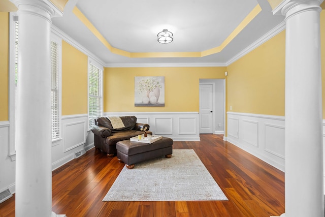 living area featuring ornate columns, a raised ceiling, dark hardwood / wood-style floors, and crown molding