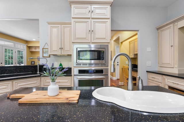 kitchen featuring stainless steel appliances, cream cabinetry, dark stone countertops, and sink