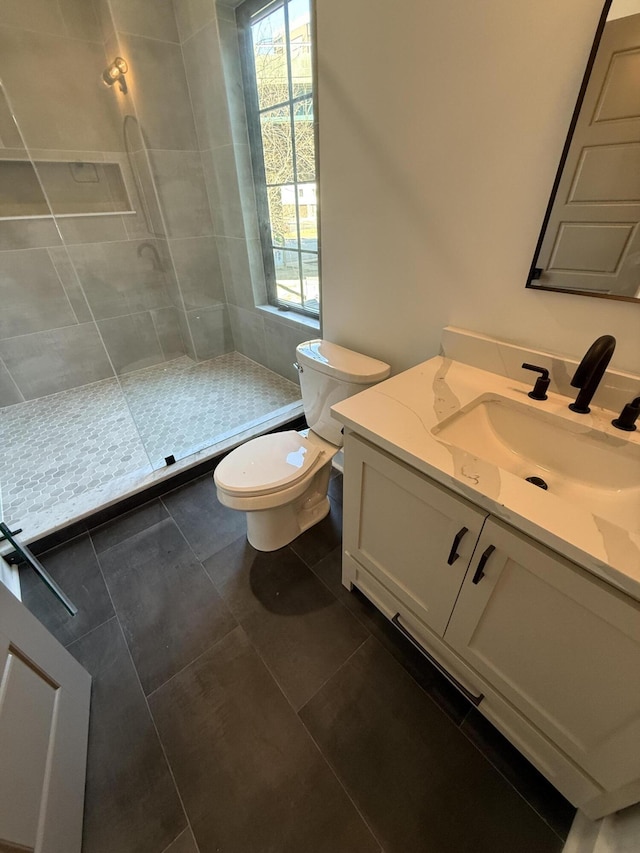 bathroom with tiled shower, vanity, toilet, and tile patterned floors