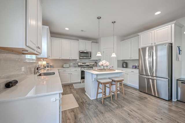 kitchen featuring pendant lighting, sink, white cabinetry, stainless steel appliances, and a center island