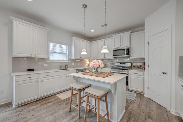 kitchen with sink, appliances with stainless steel finishes, white cabinetry, a kitchen island, and decorative light fixtures