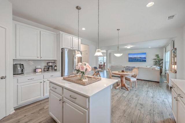 kitchen with decorative light fixtures, a center island, light wood-type flooring, stainless steel refrigerator, and white cabinets