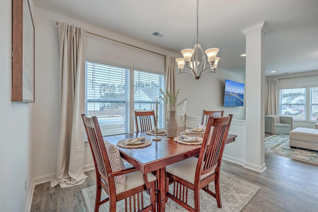 dining area with ornate columns, hardwood / wood-style floors, and a notable chandelier