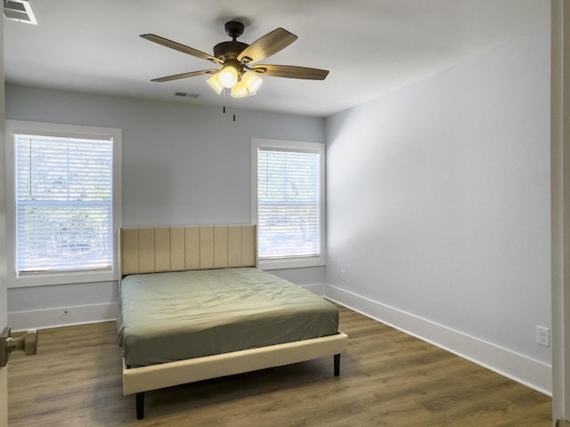 bedroom featuring ceiling fan, dark hardwood / wood-style floors, and multiple windows