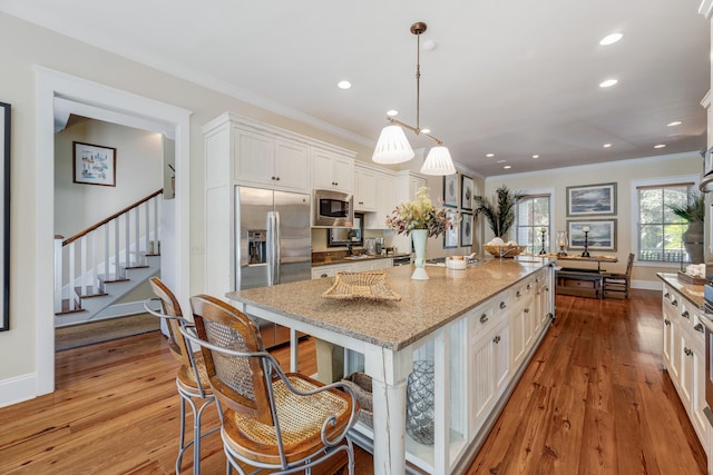 kitchen featuring light stone counters, stainless steel appliances, pendant lighting, a center island with sink, and white cabinetry