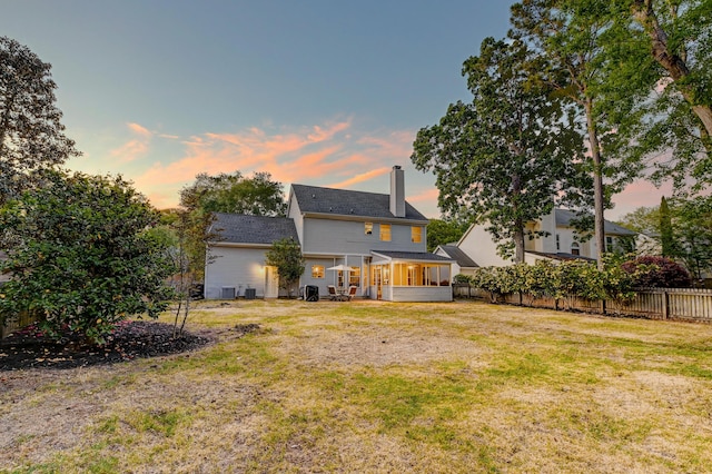 back of property at dusk with a yard, fence, a chimney, and a sunroom