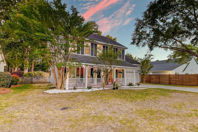 colonial house featuring fence, covered porch, driveway, and a front yard