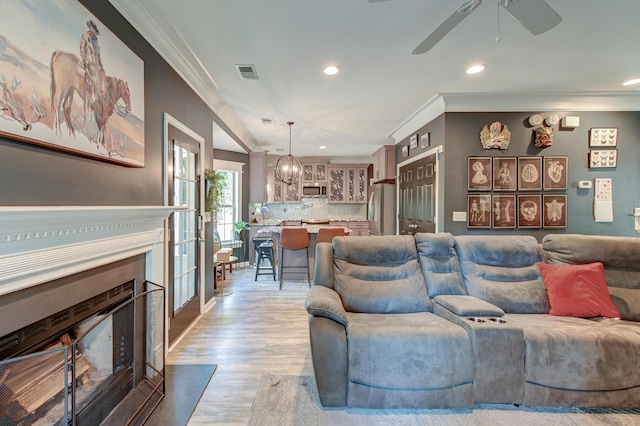 living area with crown molding, visible vents, a fireplace with flush hearth, and light wood finished floors