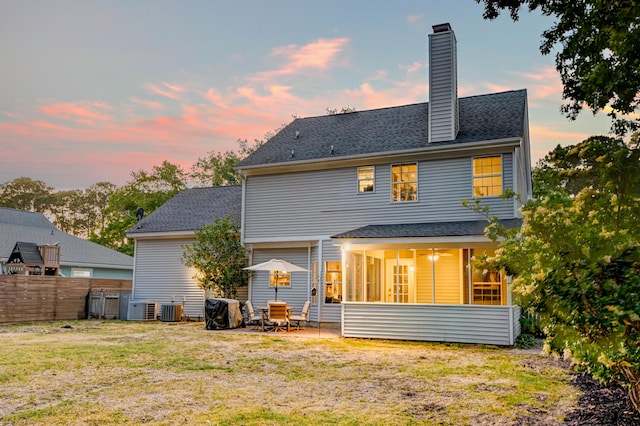 rear view of property featuring fence, cooling unit, a chimney, a sunroom, and a yard
