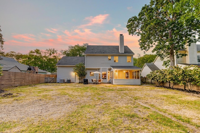 back of property at dusk with a fenced backyard, a yard, a chimney, and a sunroom
