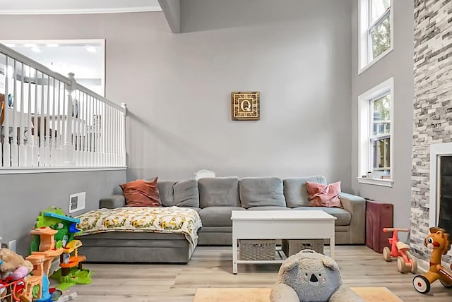 living room featuring a stone fireplace, a high ceiling, and light wood-type flooring