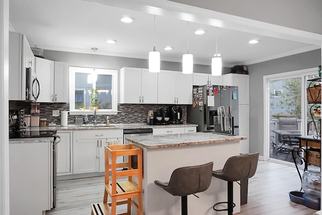 kitchen with white cabinetry, sink, stainless steel appliances, pendant lighting, and a kitchen island