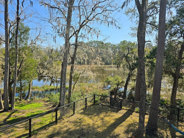 view of yard with a gate, a forest view, a water view, and fence