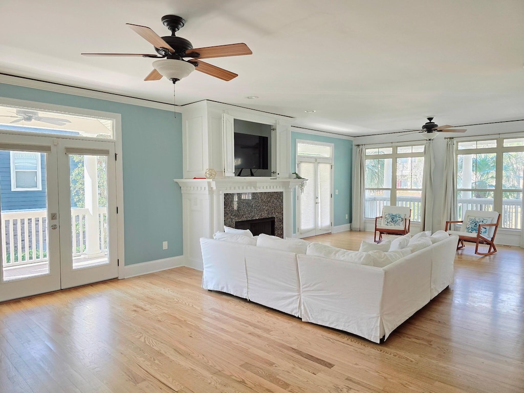 unfurnished living room with a ceiling fan, baseboards, light wood-style flooring, a high end fireplace, and french doors