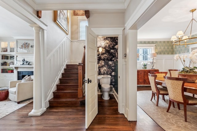 staircase with crown molding, a notable chandelier, hardwood / wood-style floors, and ornate columns