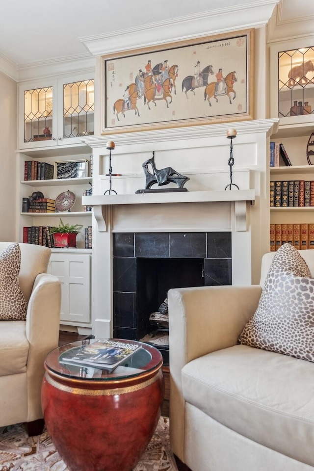 living area with a tiled fireplace, crown molding, and built in shelves