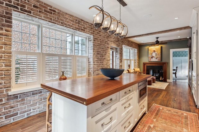 kitchen featuring hanging light fixtures, brick wall, stainless steel microwave, white cabinets, and a kitchen bar