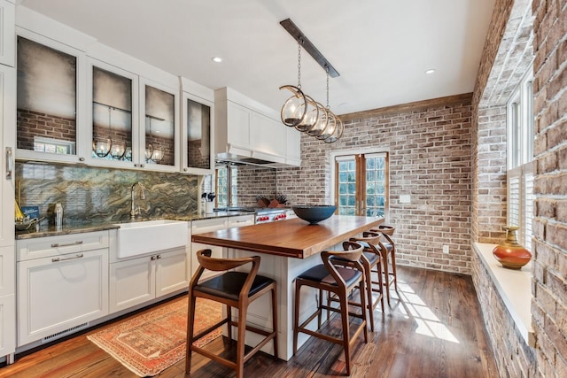 kitchen featuring a kitchen bar, dark hardwood / wood-style flooring, pendant lighting, brick wall, and white cabinets