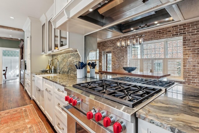 kitchen featuring white cabinetry, sink, stainless steel stove, and wall chimney exhaust hood