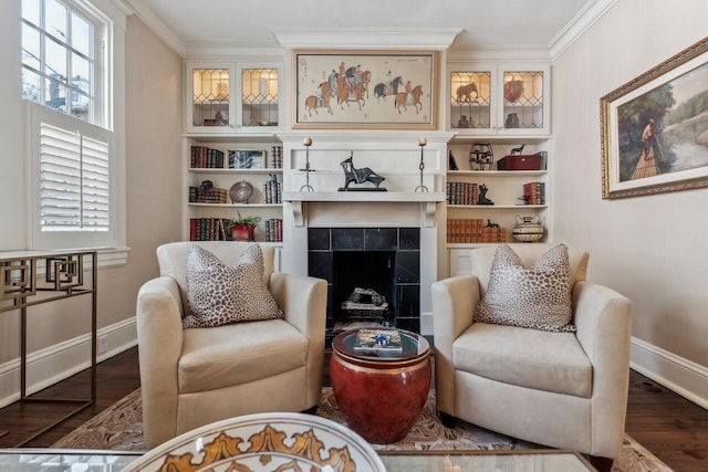 sitting room with hardwood / wood-style floors, crown molding, a tile fireplace, and built in shelves