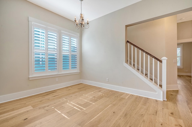 unfurnished room featuring baseboards, stairway, an inviting chandelier, and light wood-style floors