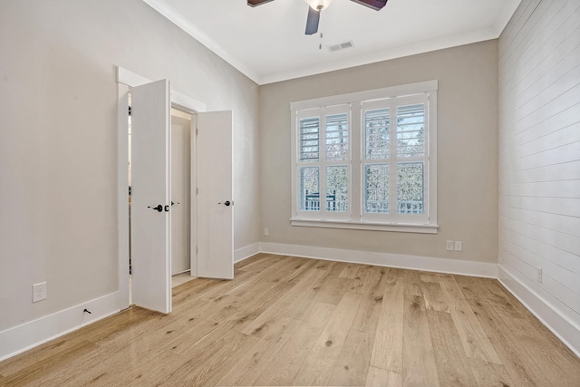 empty room featuring ceiling fan, light wood-style flooring, visible vents, baseboards, and ornamental molding