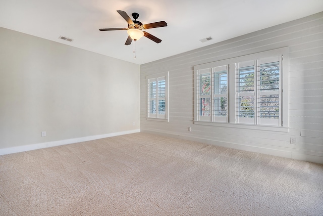 carpeted empty room featuring visible vents, wood walls, and ceiling fan