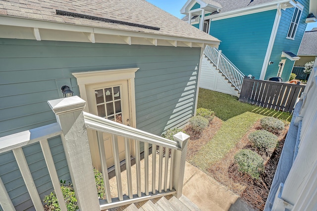 view of side of home featuring roof with shingles, fence, and stairway