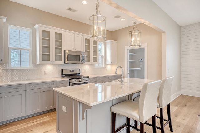 kitchen with a breakfast bar, stainless steel appliances, tasteful backsplash, visible vents, and gray cabinetry