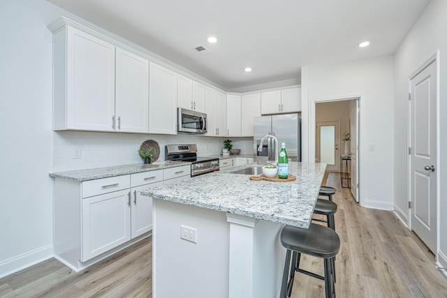 kitchen with appliances with stainless steel finishes, white cabinets, a kitchen bar, light stone counters, and a center island with sink