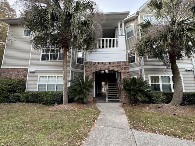 view of front facade with stairway, brick siding, a balcony, and a front lawn